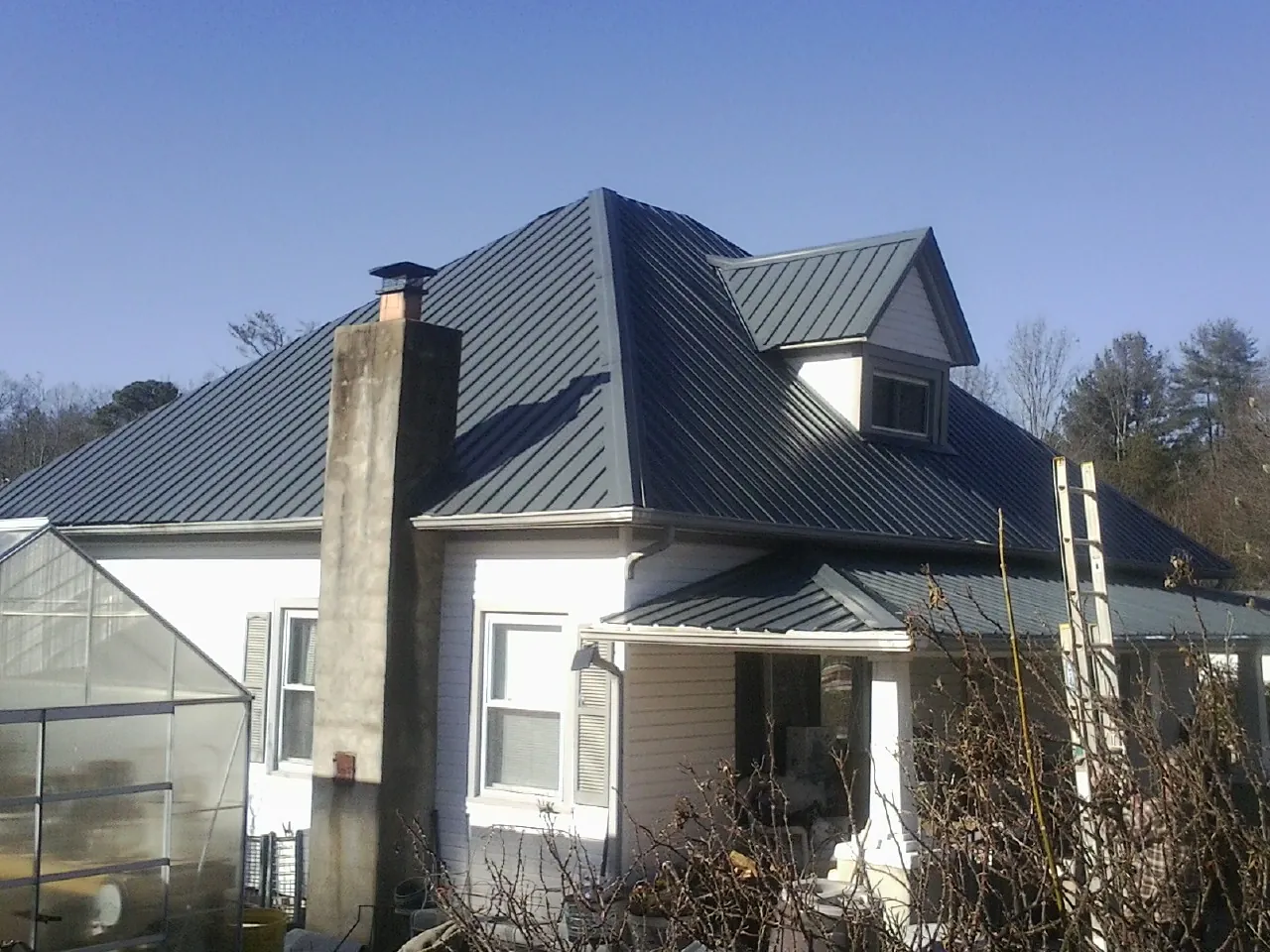 Dark blue standing seam metal roof on a white farmhouse with dormer in Henderson