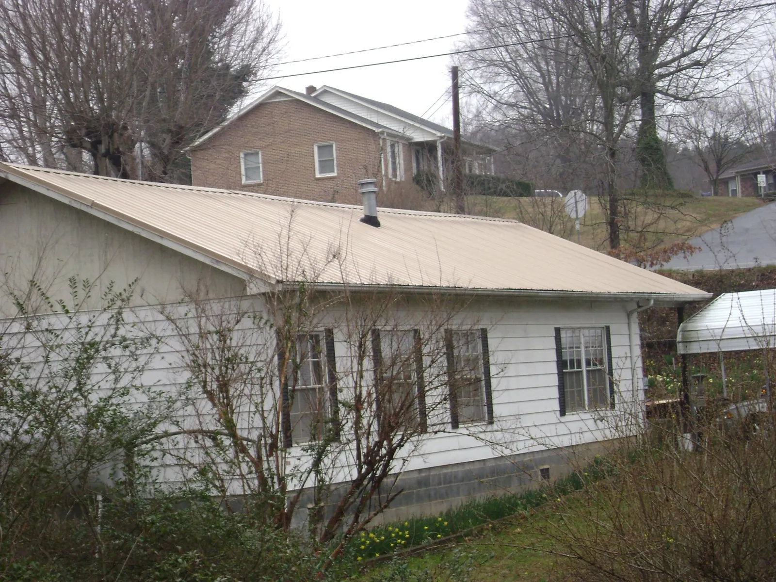 Tan metal roof on a white sided house set into a hillside — Commercial Roofing by Roofing Brothers in Henderson